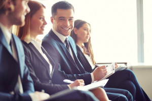 Row of business people making notes at seminar with focus on smiling young man