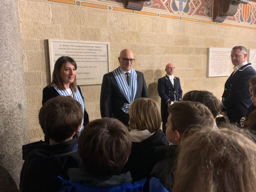 Gli Eccellentissimi Capitani Reggenti Francesca Civerchia e Dalibor Riccardi si fermano a salutare le bambine e i bambini delle classi V di Fiorentino, V di Falciano e VB di Borgo Maggiore mentre escono da Palazzo Pubblico per recarsi in Basilica.